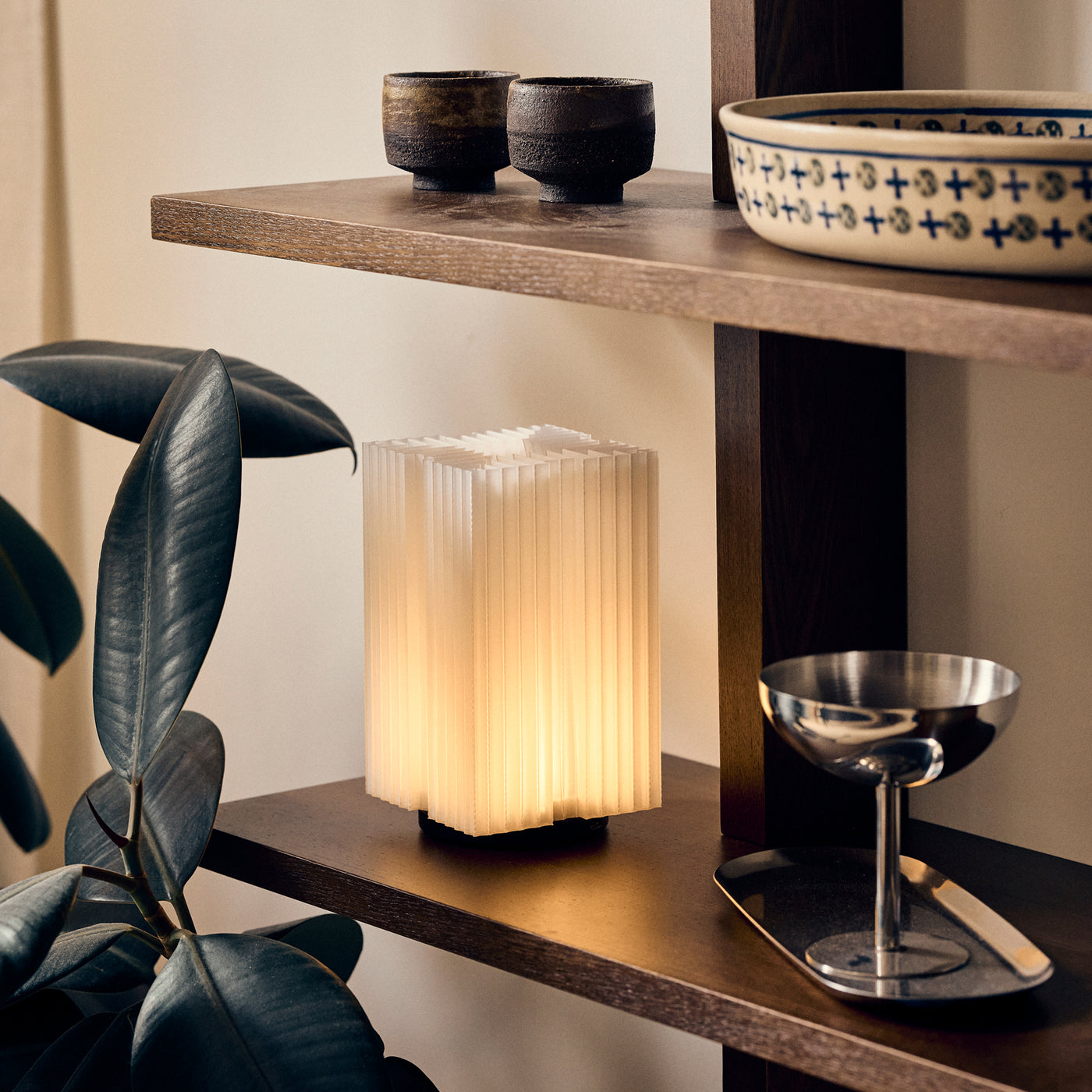 Cordless mini brut lamp in natural on shelf next to rubber tree