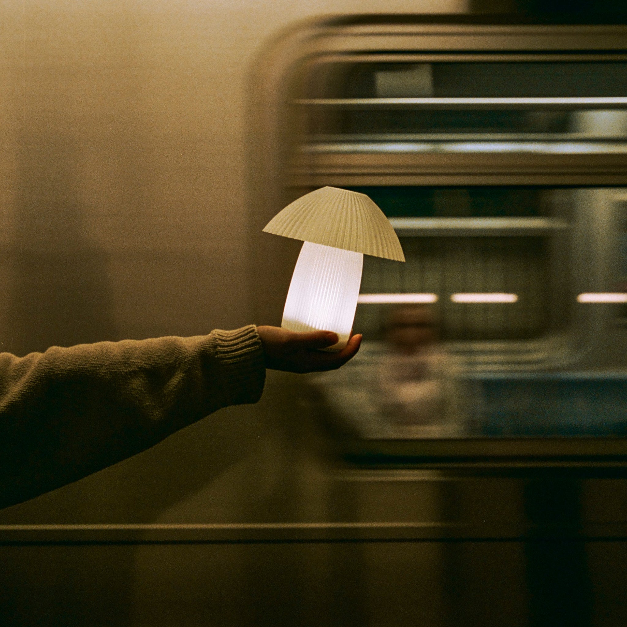 Hand holding Kinoko cordless lamp as subway passes behind