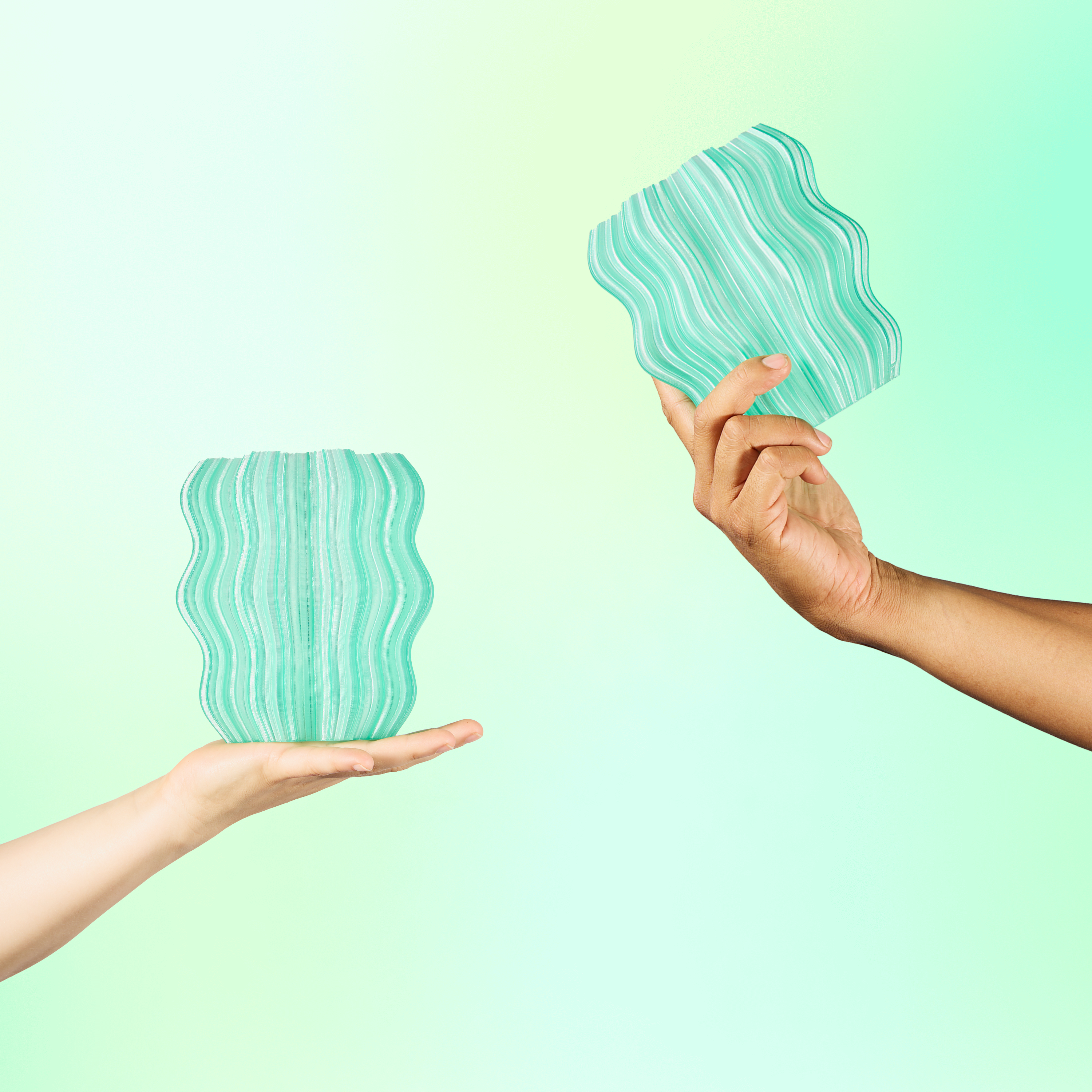 Two hands holding two seafoam Mini Wavy Lamps on green background