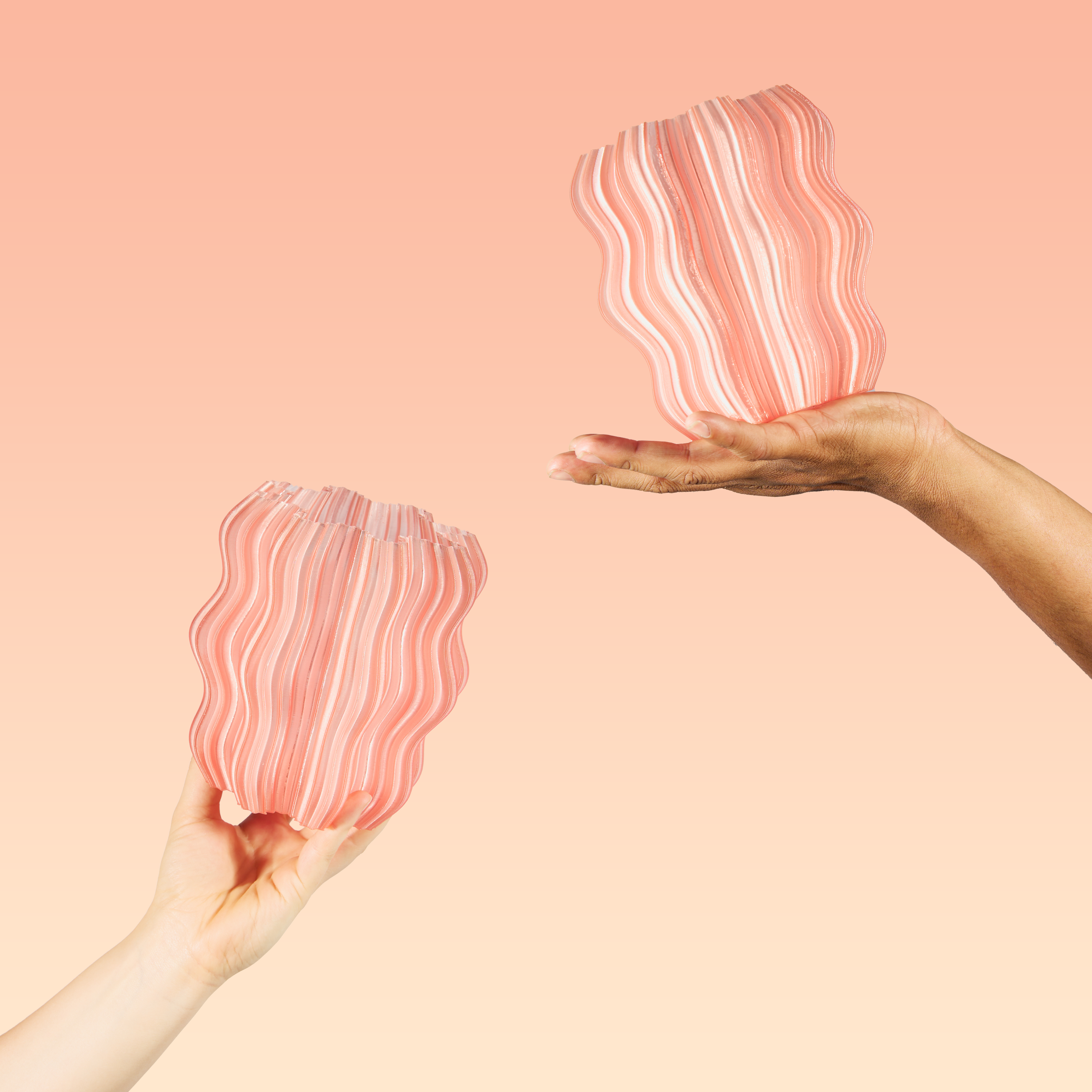 Two hands holding two peach Mini Wavy Lamps on orange background