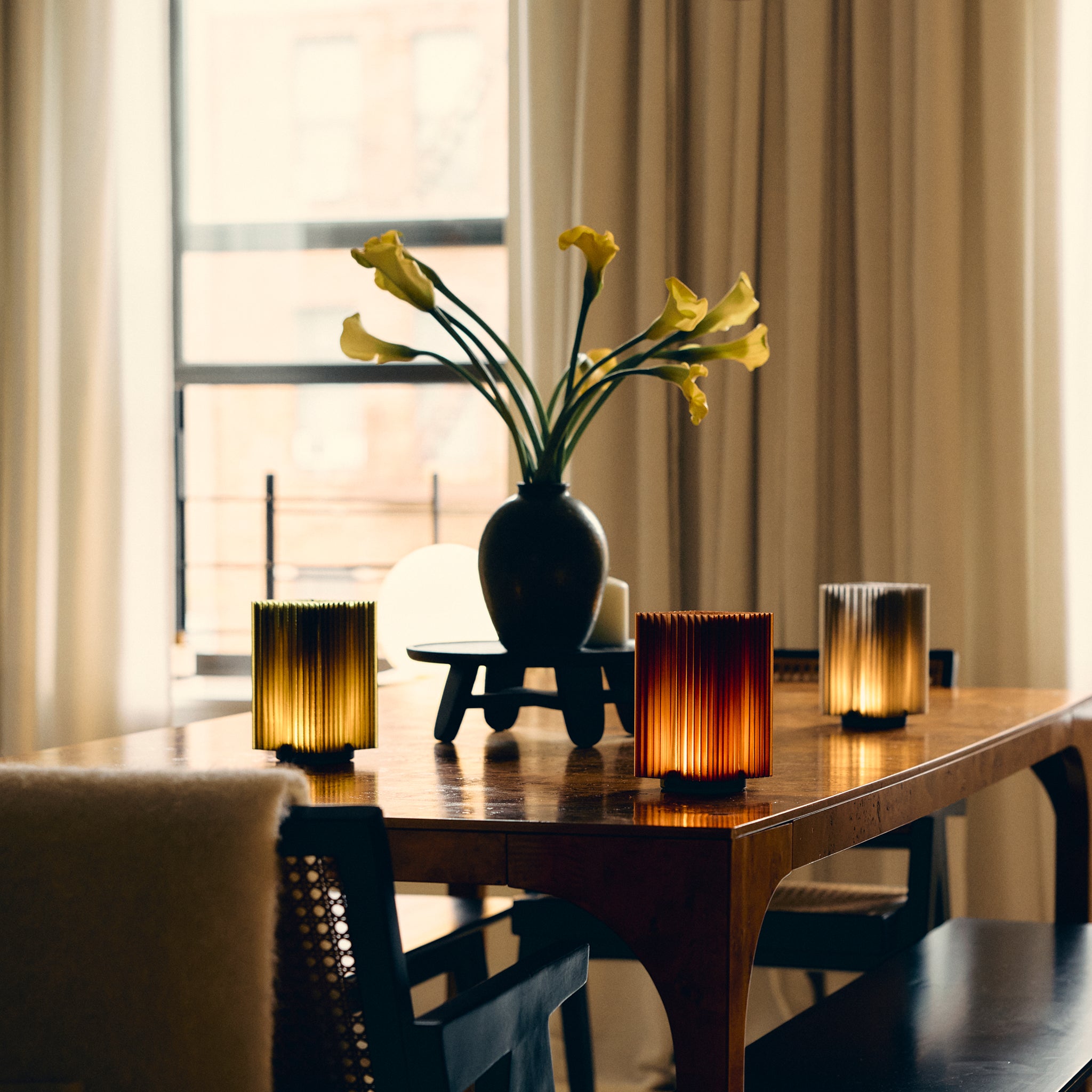 Cordless mini brut lamps in smoke, olive oil, and amber on dining talbe with flowers.
