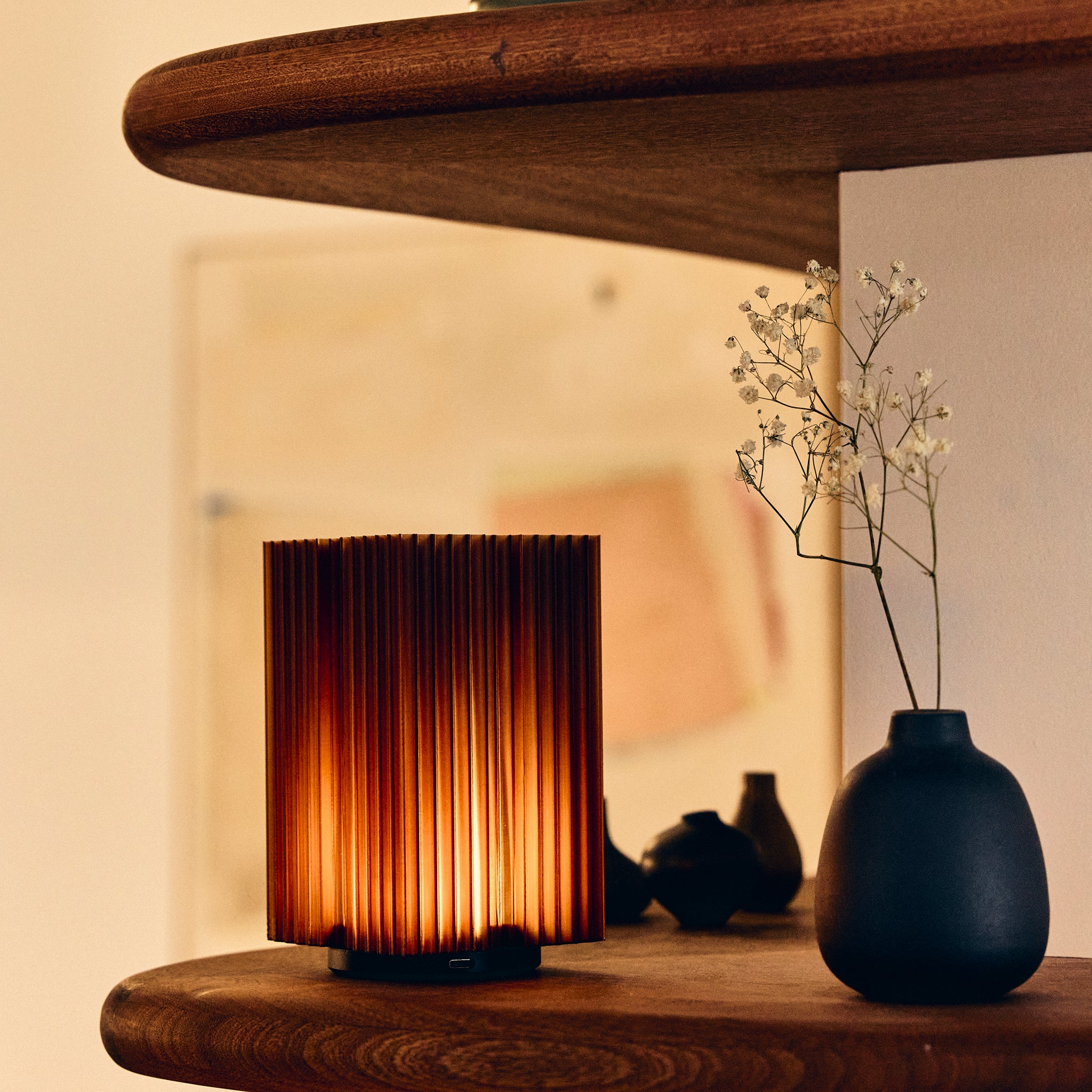 Cordless mini brut lamp in amber on wooden shelf next to black vase