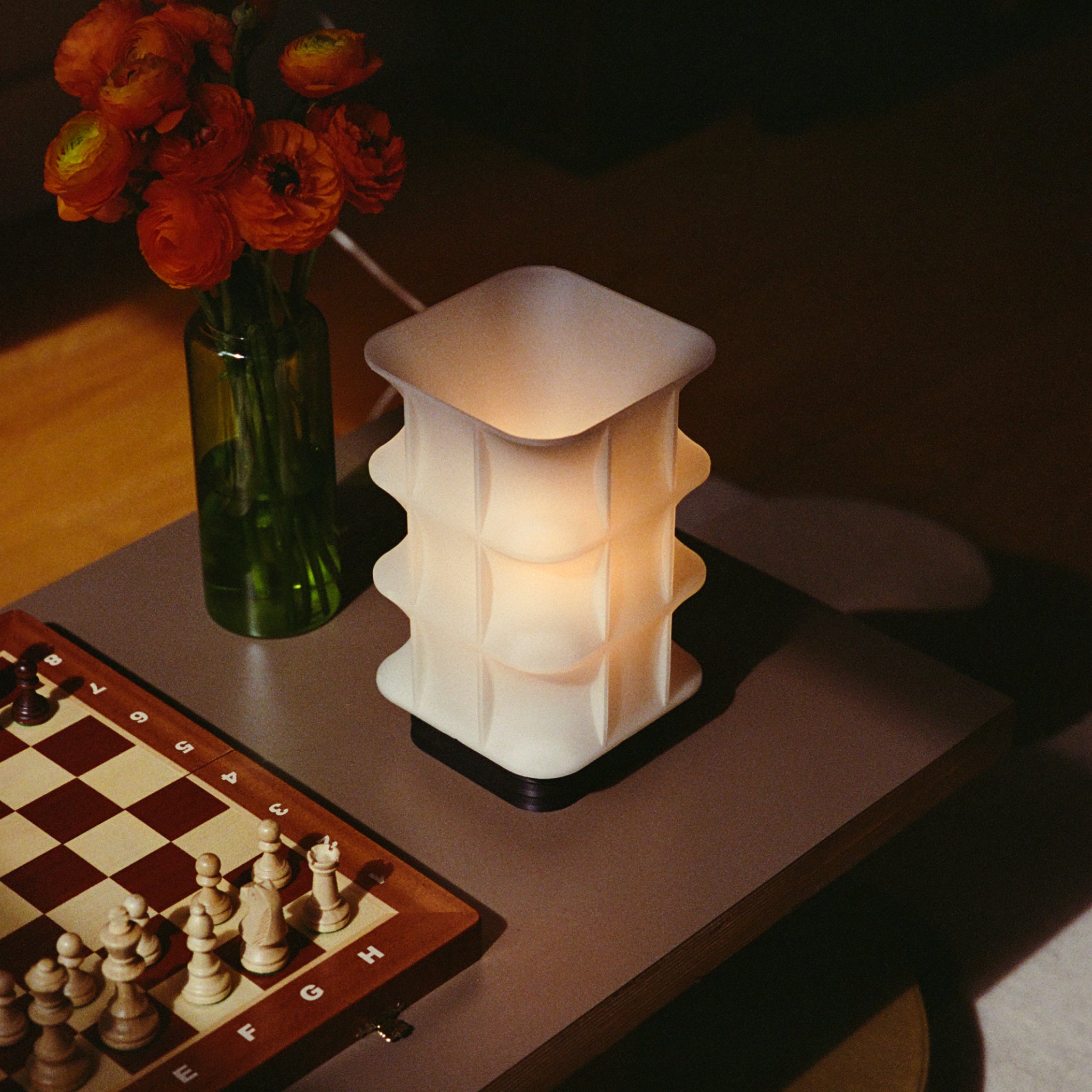 Image of Scaffold Lamp with a warm glow next to a chess board