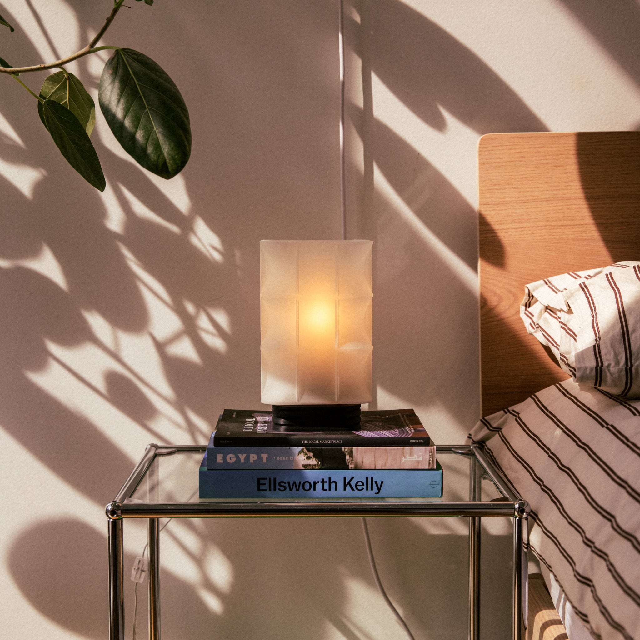 Image of Scaffold Lamp next to a bed on a glass nightstand