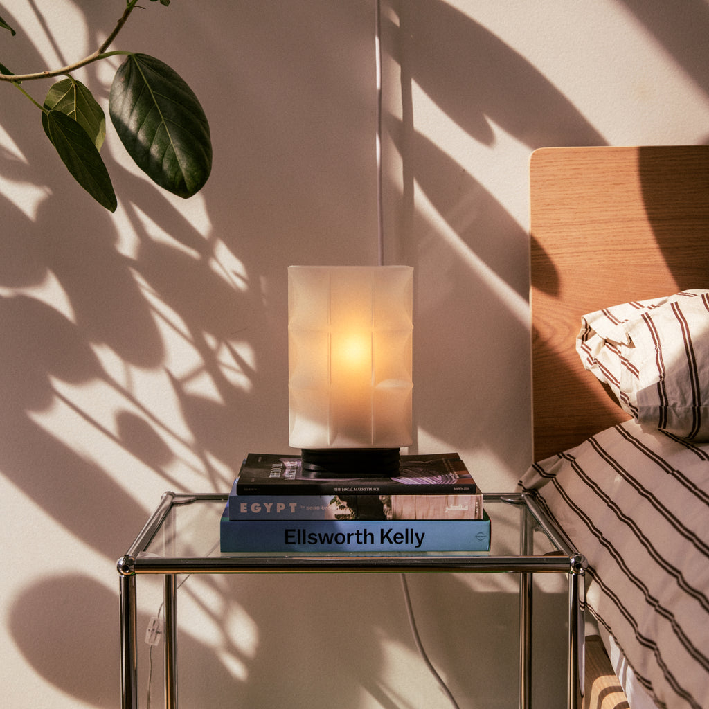 Image of Scaffold Lamp next to a bed on a glass nightstand