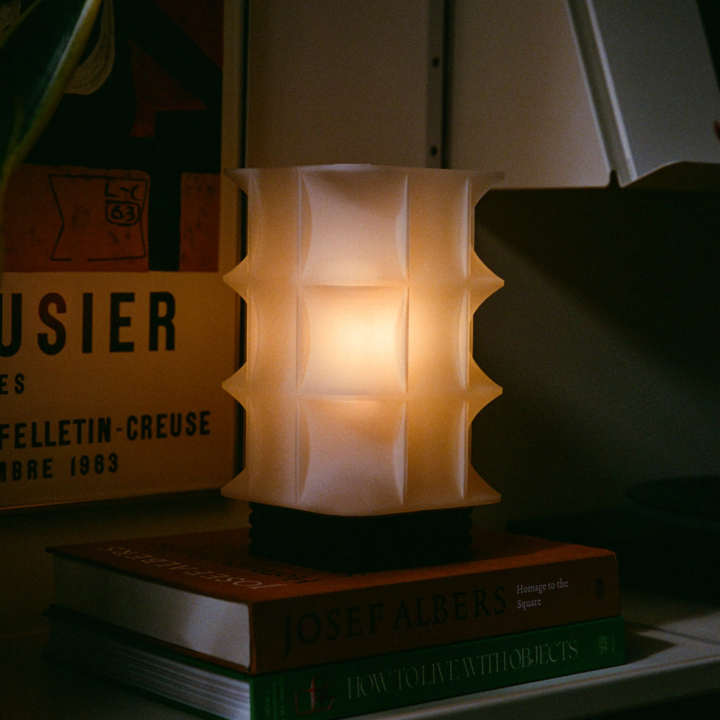 Image of Scaffold Lamp with a warm glow on a bookshelf