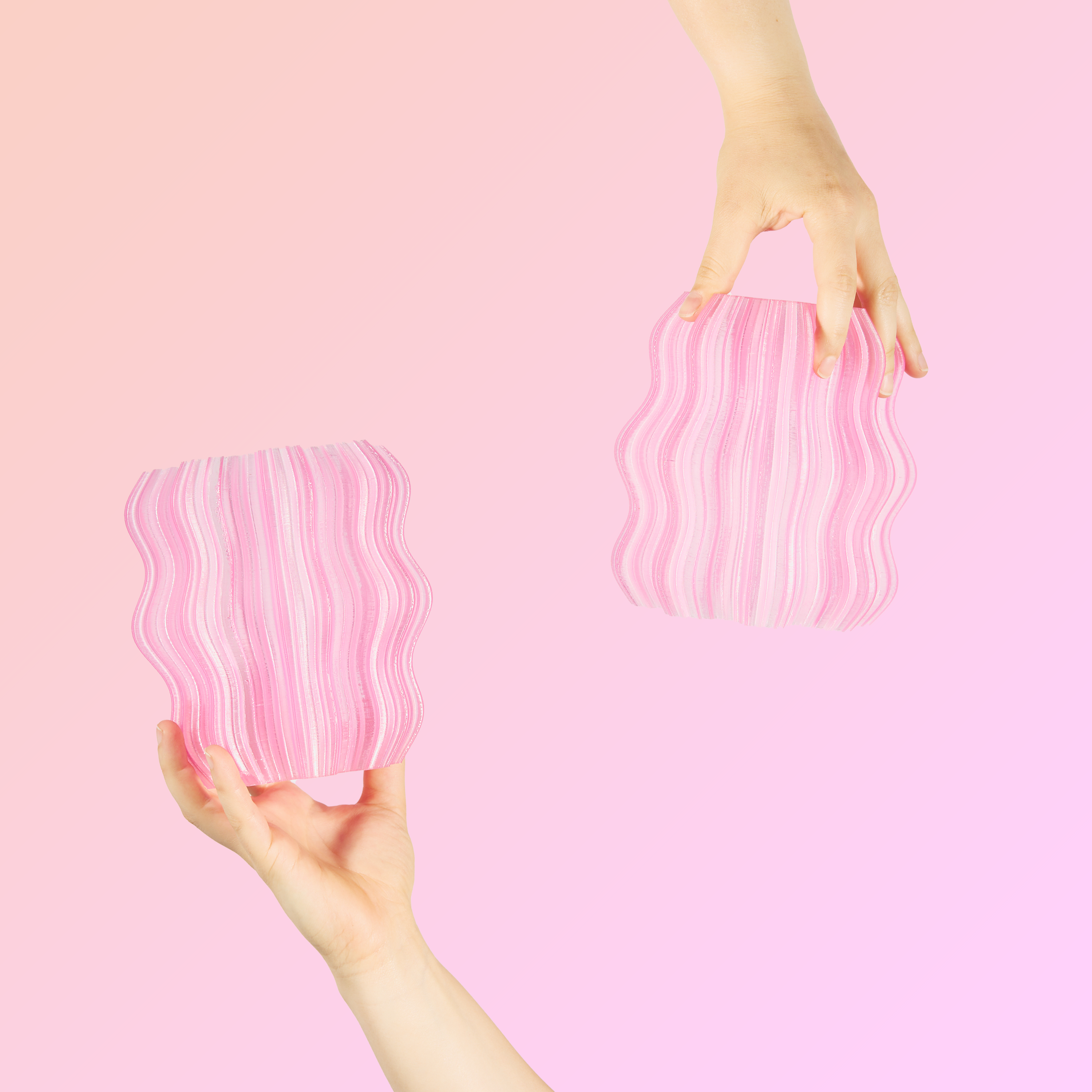 Two hands holding two pink Mini Wavy Lamps on pink background